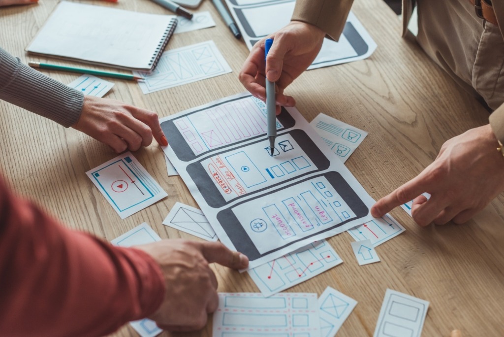 Cropped view of designers working with app sketches and template of mobile website at table