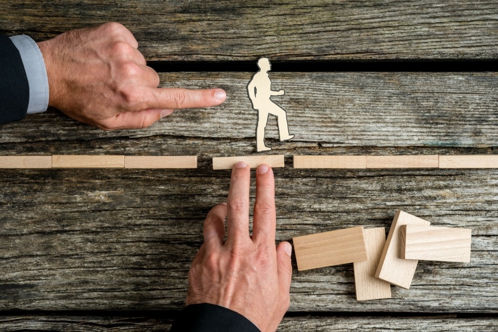 Two businessmen supporting and giving a helping push to silhouette cutouts of a man